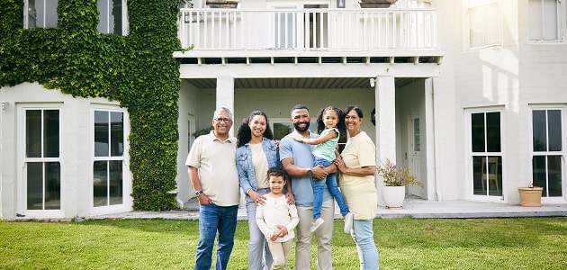 Multi-generational family smiling in front of a large home, representing wealth management services for high-net-worth families offered by Polymath Investments.