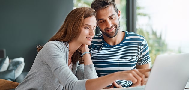 Young couple smiling while exploring investment options on a laptop, reflecting approachable financial planning.
