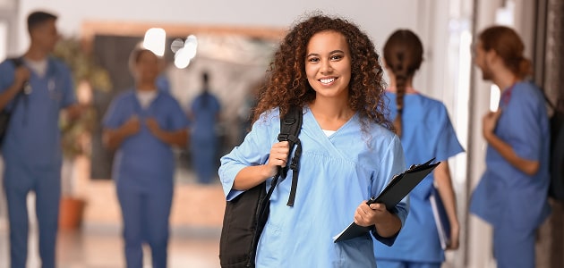 Smiling medical resident in scrubs holding a clipboard and backpack, representing Polymath Investments’ financial planning services for early-career physicians.