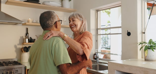 Older couple smiling and embracing in a sunlit kitchen, conveying financial peace of mind during retirement—a key focus of Polymath Investments.