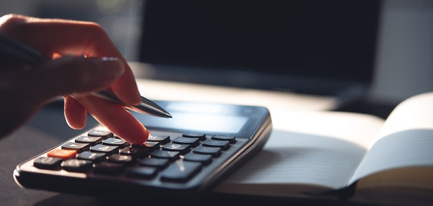 Hand using a calculator with a notebook, representing detailed financial planning and budgeting.