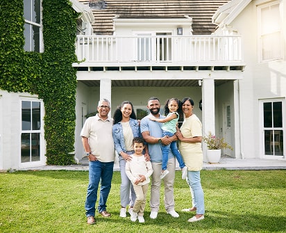 Multi-generational family smiling in front of a large home, representing wealth management services for high-net-worth families offered by Polymath Investments.