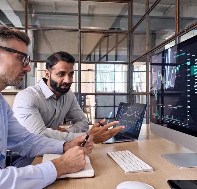 Two professionals reviewing investment charts on a large monitor, representing Polymath Investments’ data-driven financial planning and investment management.
