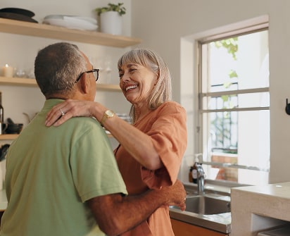 Older couple smiling and embracing in a sunlit kitchen, conveying financial peace of mind during retirement—a key focus of Polymath Investments.